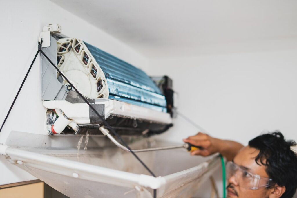 A man repairs an air conditioner, using tools and focused on the unit.