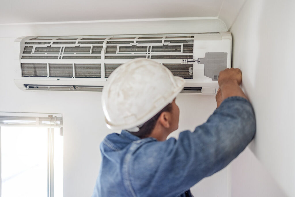 A man wearing a hard hat works on fixing an air conditioning unit.