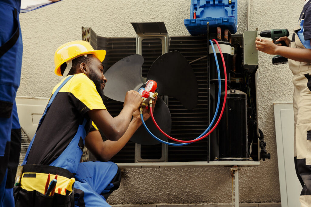 Three men repairing an air conditioner together in a residential setting.